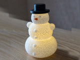 Schneemann mit Hut und Nase über einem LED-Teelicht